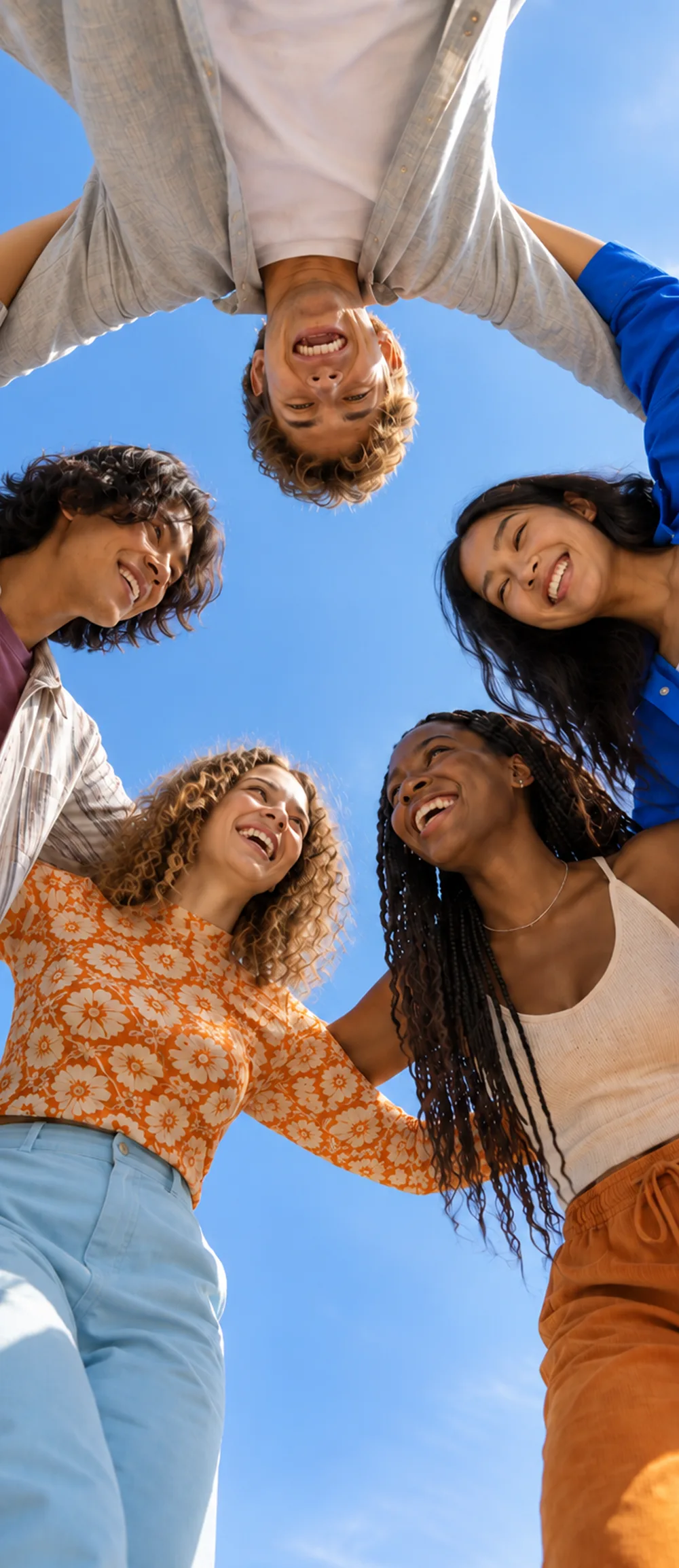 A group of friends laughing together with their arms around each other under a blue sky